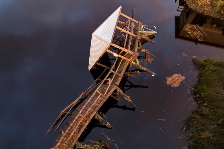 an overhead view of a toppled wooden dock and structure against a dark body of water