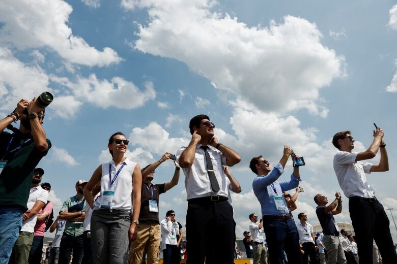 Visitors watch air show near Paris, with some taking photos while others plug their ears.