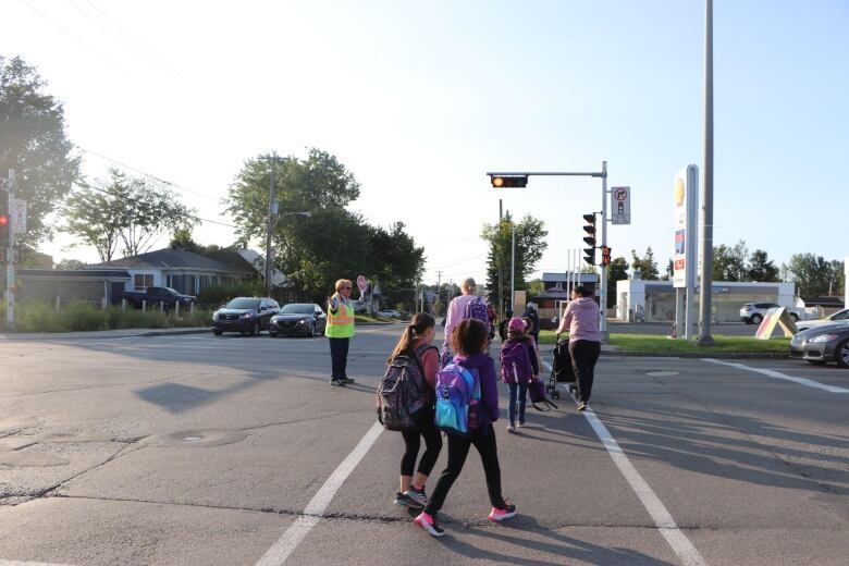 A woman leads a group of children across the street 