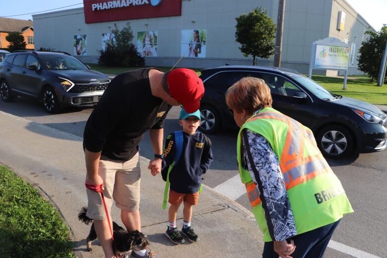 A woman in a yellow vest bends down to talk to a child accompanied by his father.