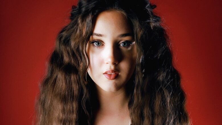 A girl with big crimped hair poses in front of a red background