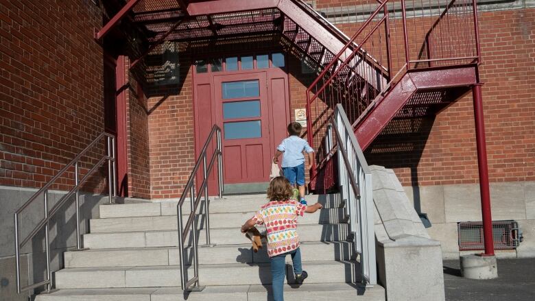 Kids walk up a staircase into a brick building.