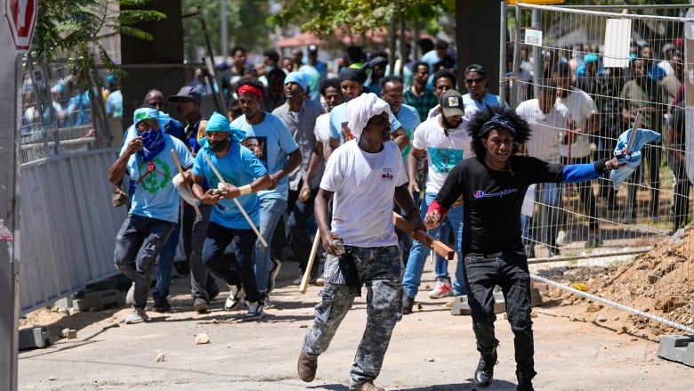 Men carry sticks and run during a protest.