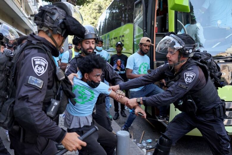 Police pull a man's shirt and arm while they arrest him near a bus.