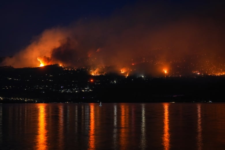 A wildfire rages on mountains above a lake.