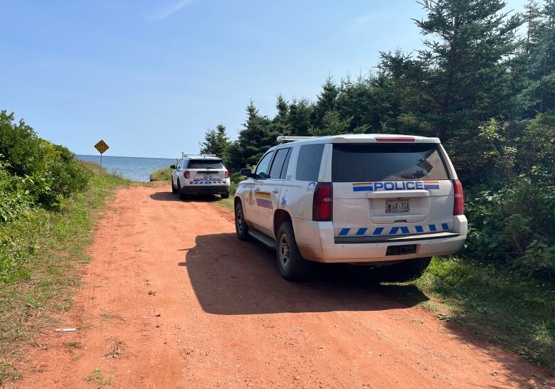 Police cars on red dirt road.