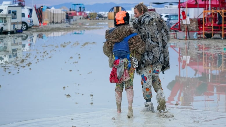 Two people walk through muddy grounds.