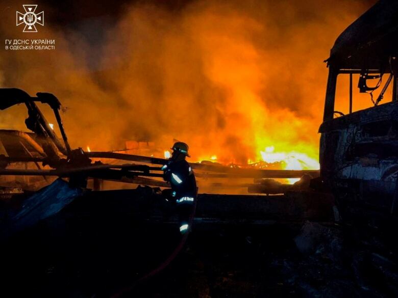 A firefighter works at a burning site and near destroyed vechicles.