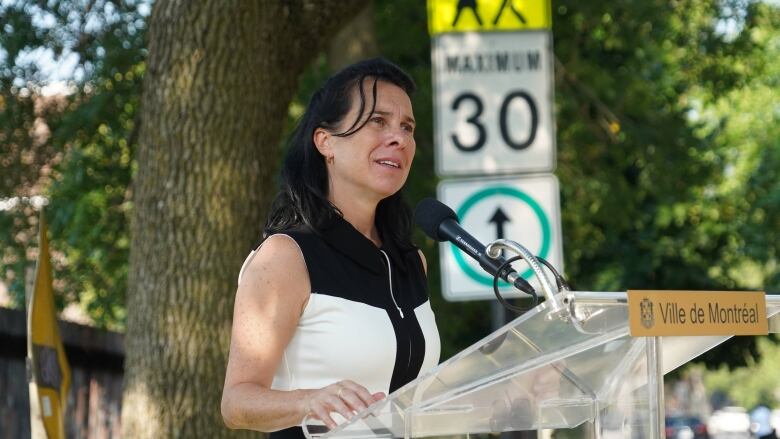 Montreal's mayor speaks at a podium in front of a 30 km/h sign. 