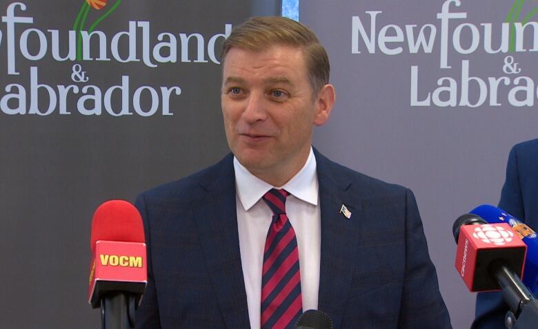 A man wearing a dark blue suit standing behind microphones. 