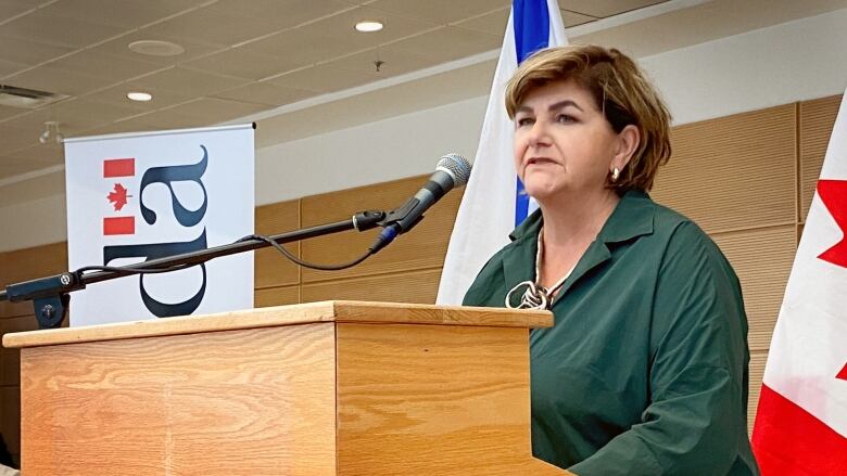 A woman in a green dress stands at a podium and speaks into a microphone.