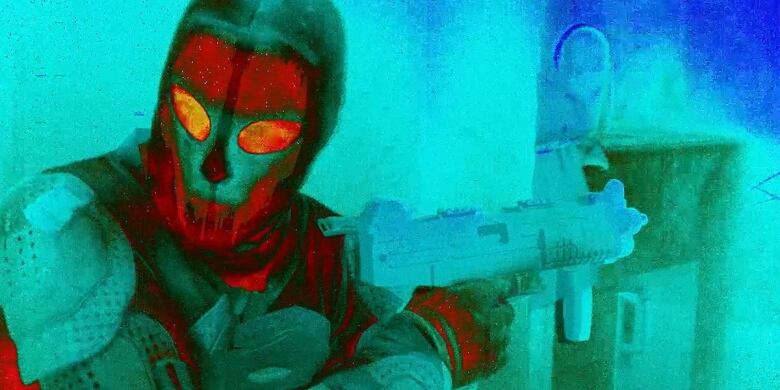 Closeup of a figure wearing a mask and holding a gun, shot in infrared so that the colours appear to be inversed and glowing. Shades of aqua and red.