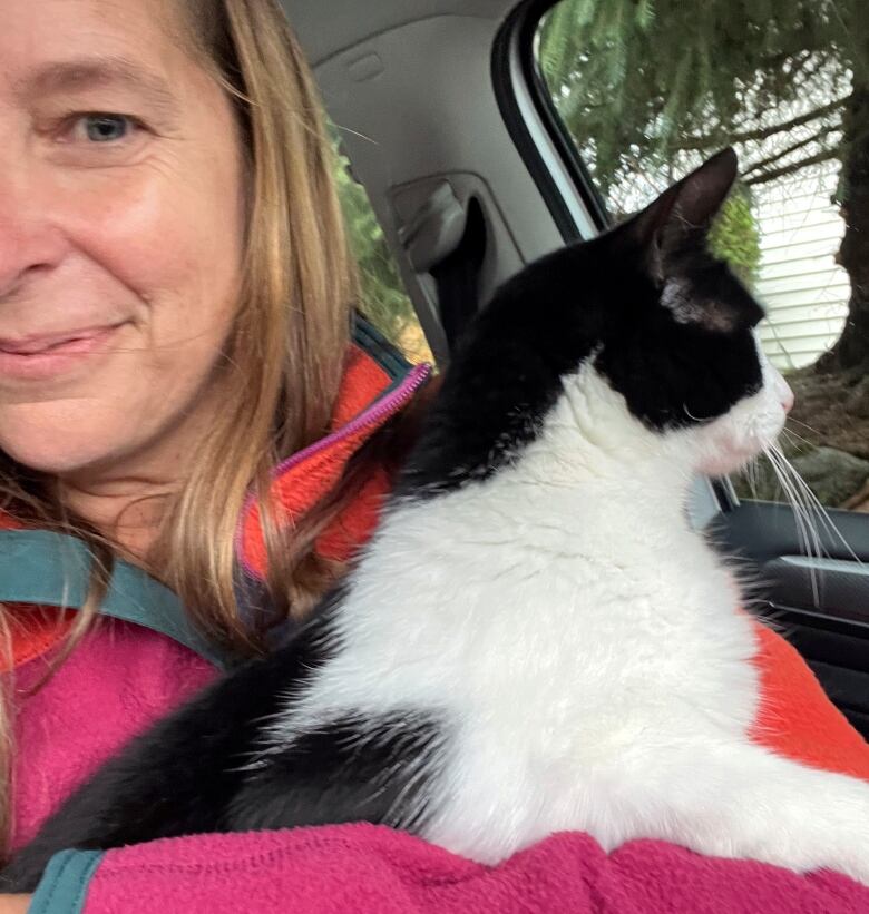 A woman sits in a vehicle with a black-and-white cat in her arms.