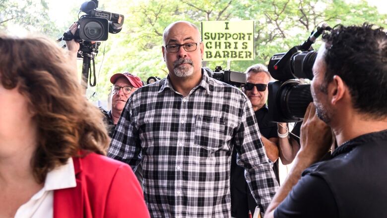 A man in a plaid shirt and glasses walks toward a courthouse on a summer morning.