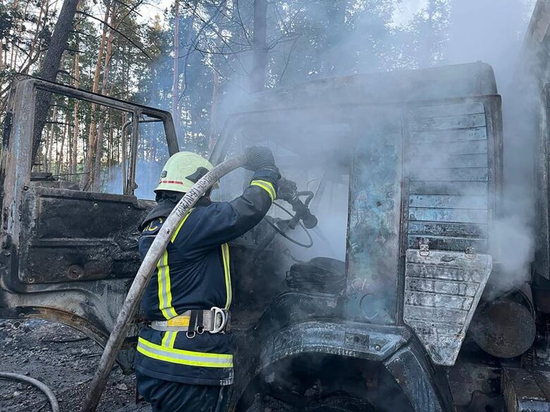 A firefighter sprays water on a vehicle following a Russian attack on Kyiv.