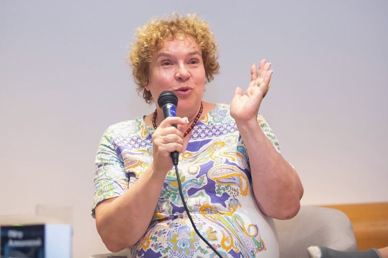 A  woman in a paisley top speaks  into a microphone.