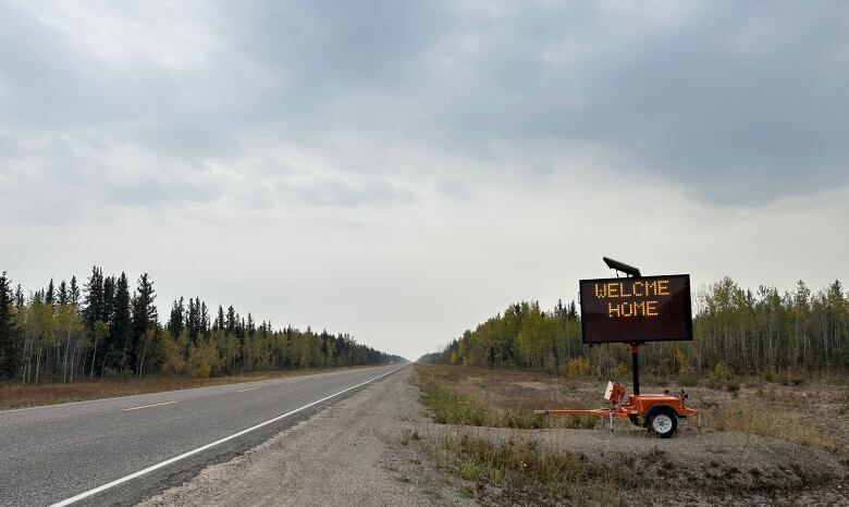 A road with a sign on the shoulder that says: Welcome Home