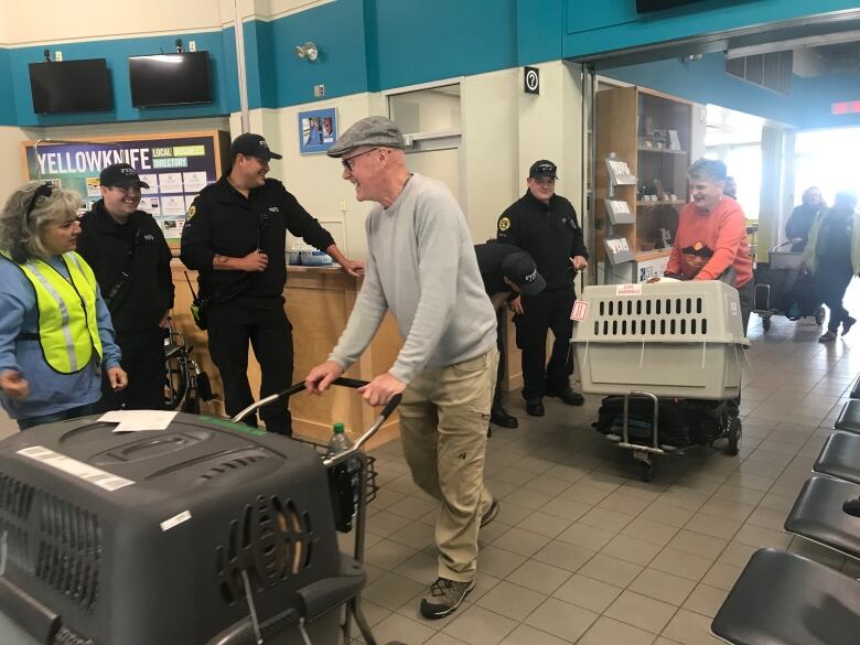 People at airport, pushing pet crates, smiling. 