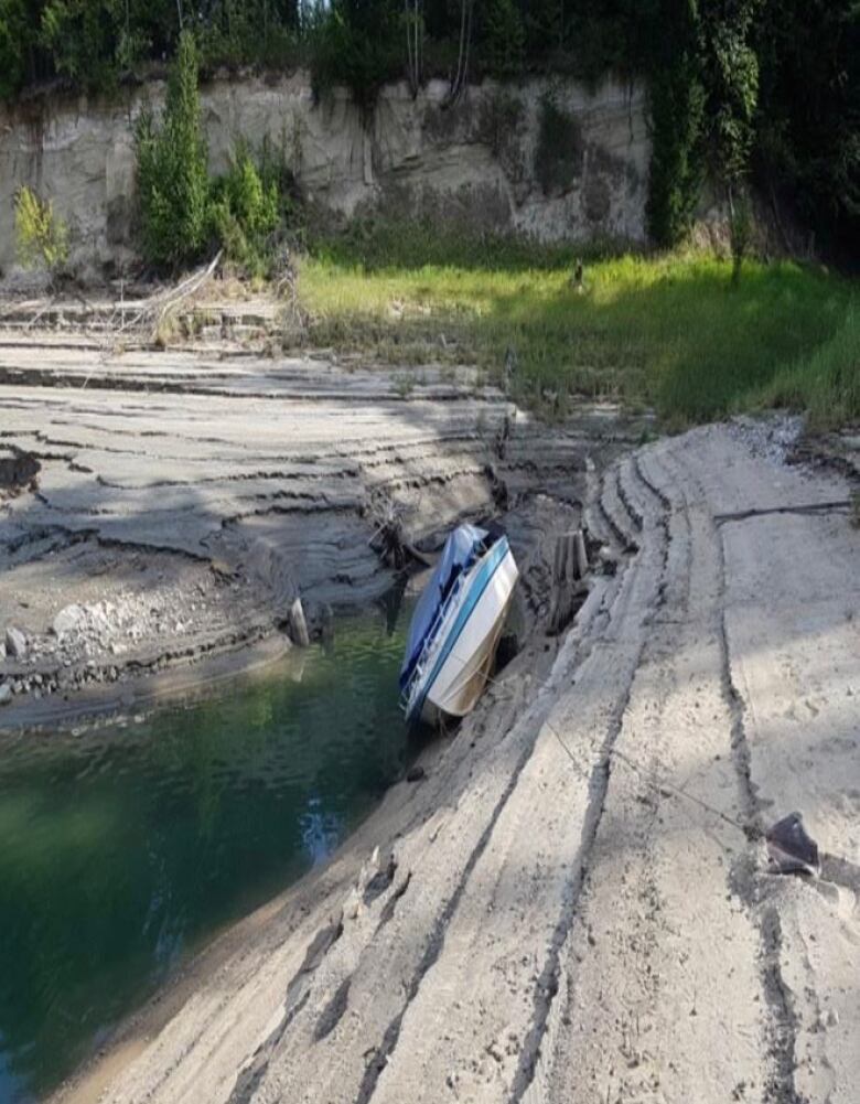 A boat hangs precariously on the side of a lake bottom that has been dry.