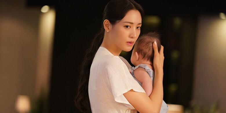 A young Korean woman in a white shirt holds her young baby.