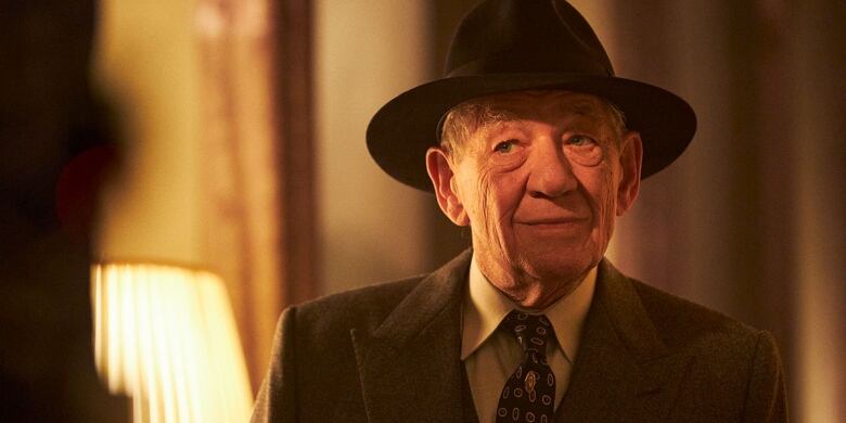 Film still Ian McKellen in a brown suit and tie with a black wide-brimmed top hat.