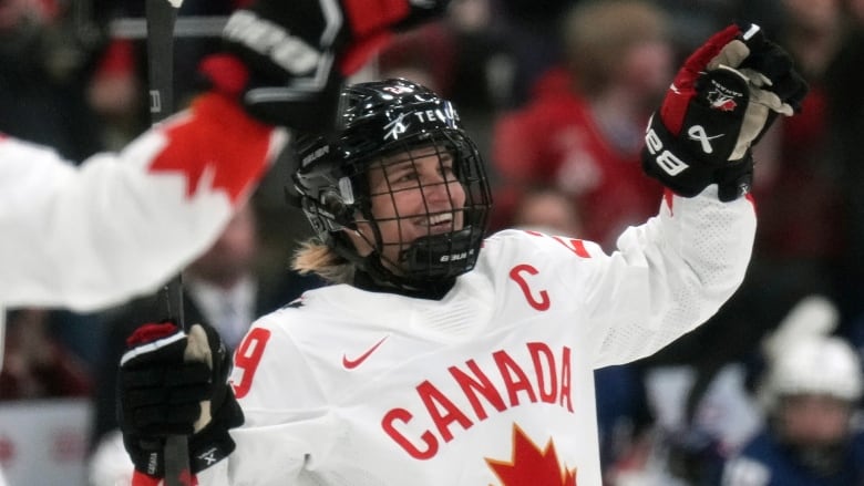 A hockey player lifts up her arms in celebration.