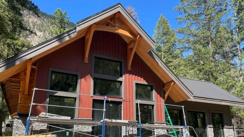 A nearly finished cabin with many windows in the woods with construction materials lying around scaffolding at the front. 