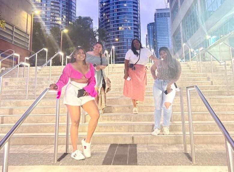 Four women stand on steps with a city scape behind them.