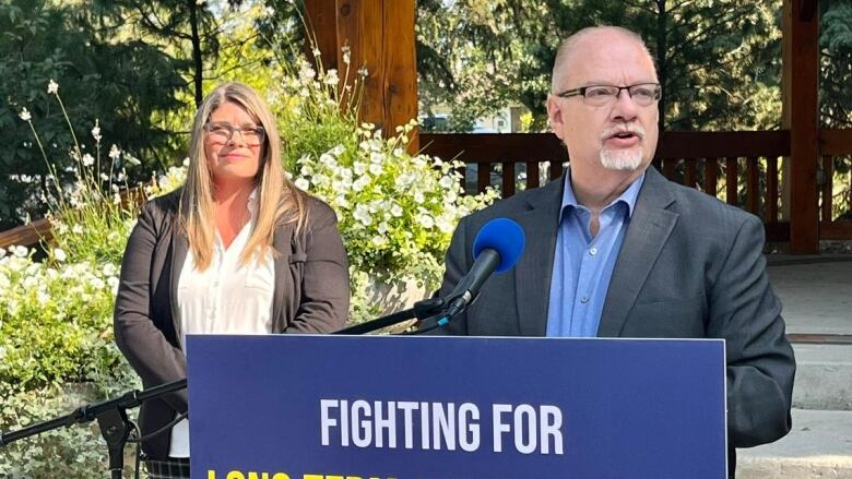 A politician makes an announcement in front of a lectern with a sign that reads 'Fighting for long-term affordability.'