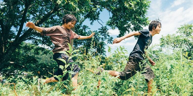 Two smiling boys leap through the grass. 