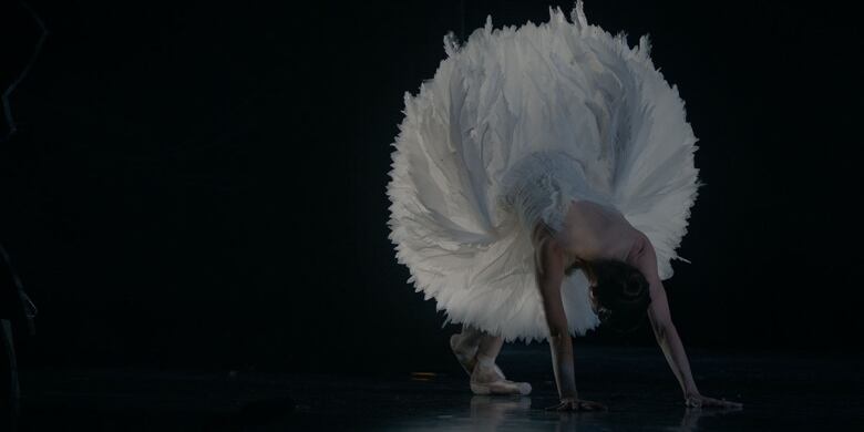 A ballerina on stage leans over, stretching her legs. 