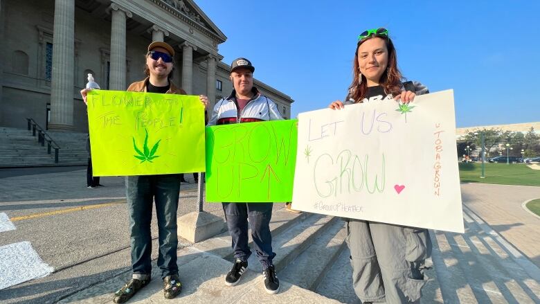 Three people stand next to each other holding posters. One poster says 