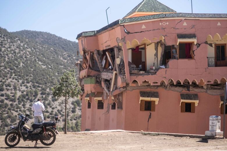 A man stands beside a building damaged by an earthquake.