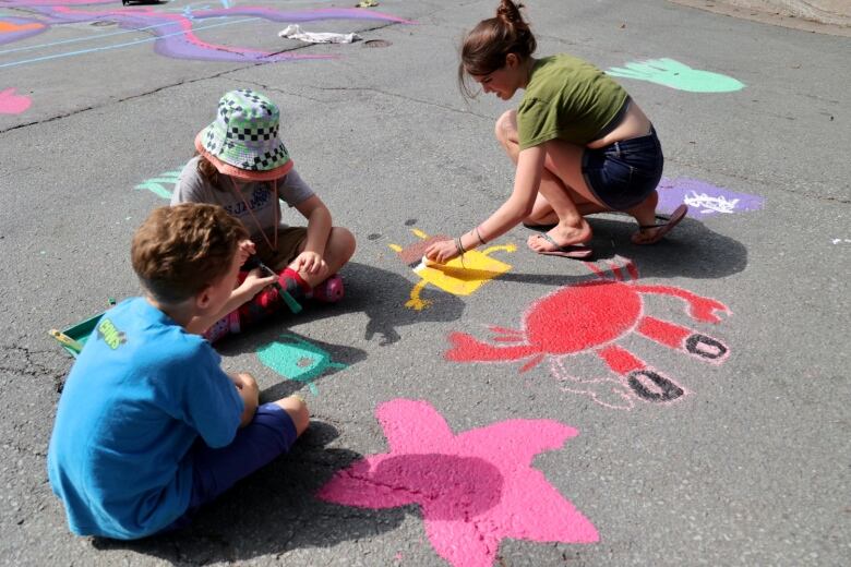 Three children are seen painting colourful characters on a street.