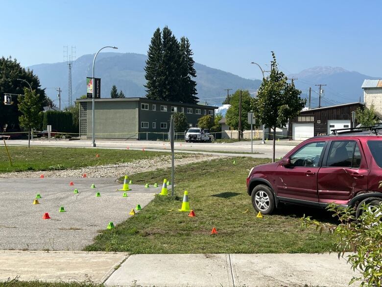 A red SUV with a large dent sits on the lawn with a police truck in the distance.