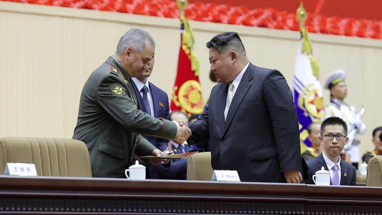 A man in a suit and tie shakes hand with an older man in a military uniform jacket.