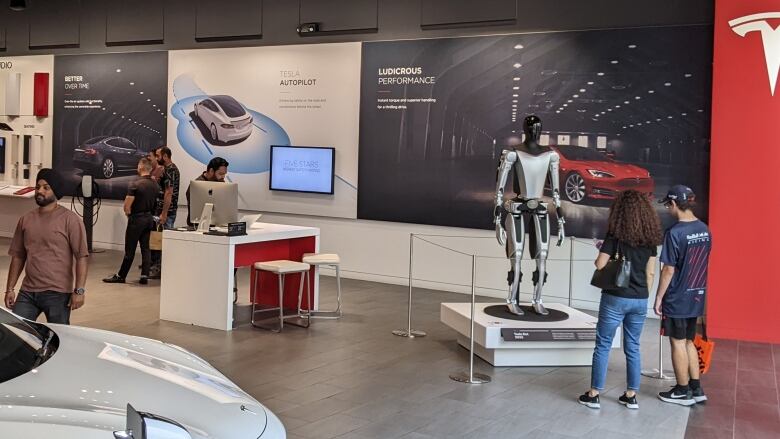 Shoppers admire a model of the Tesla humanoid robot at the automobile showroom in Toronto's Sherway Gardens. Tesla robot wide shot, Sherway Gardens, Toronto