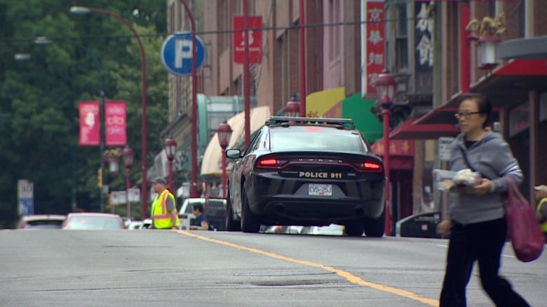 A black sedan reading 'Police 911' on the rear bumper is stopped on a Chinatown street, with red lampposts and Chinese language signs in the background.