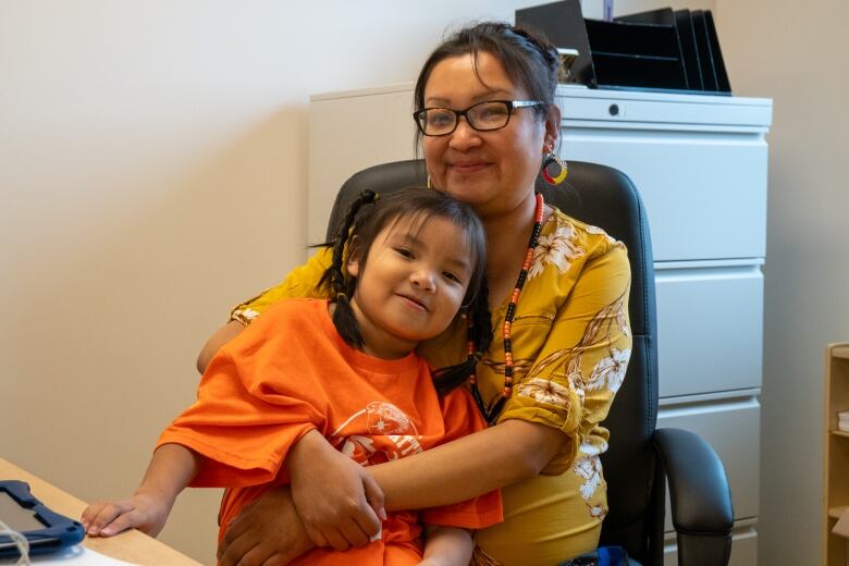 A woman sits at a desk with a child sitting on her lap.