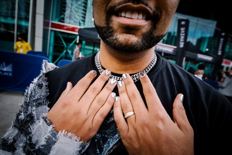 A man shows off silver-painted nails and a chain.