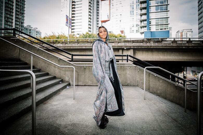 A Black woman, dressed in silver from head to toe, poses on a set of stairs.