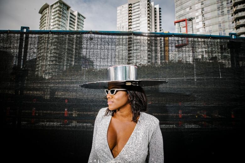 A Black woman wearing a silver top and a large silver hat is pictured in profile.