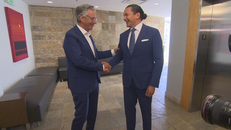 Two politicians in blue suits shake hands.