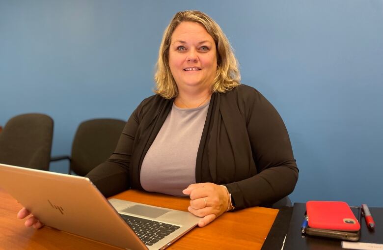 Tara Ferguson, Health PEI's Director of Infection Prevention and Control, works at her laptop, with a pile of folders and a pen situated next to her. 