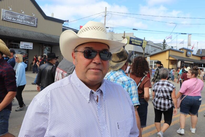 A man wearing plaid and a cowboy hat looks at the camera. 