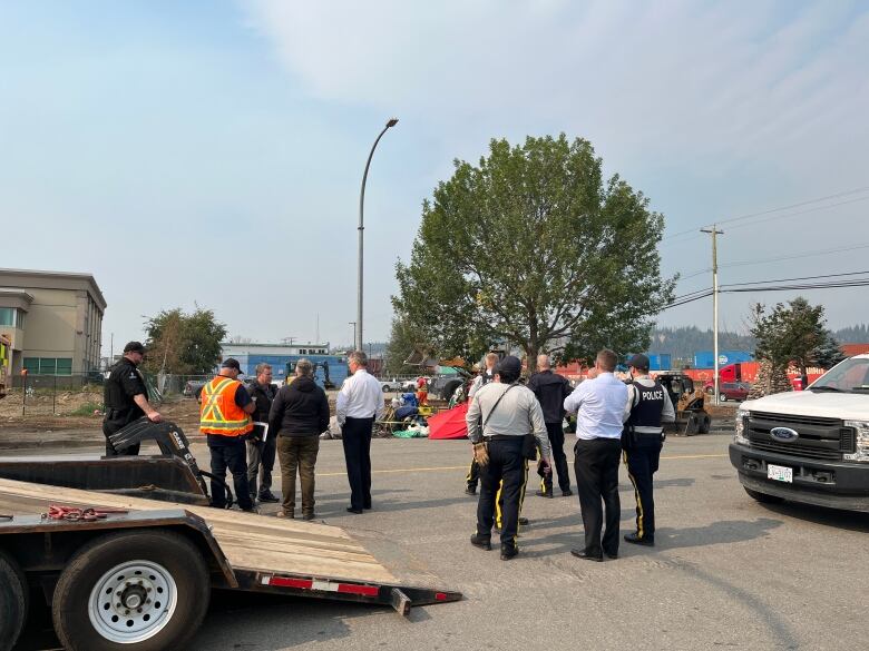 RCMP and bylaw officers stand in front of partially demolished encampment