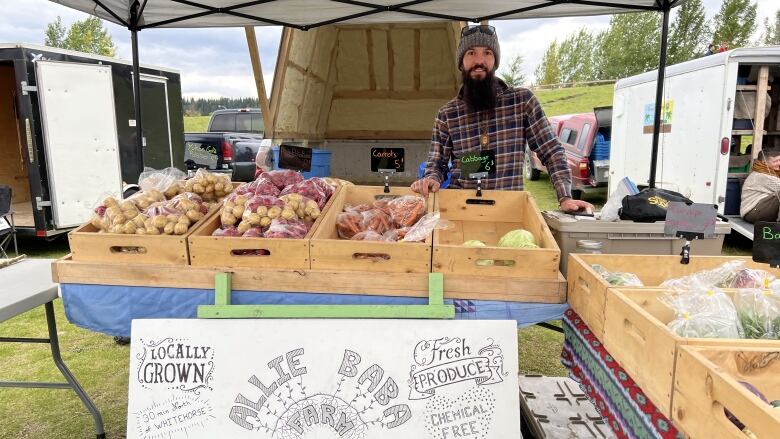 A man stands behind a table with crates of produce.