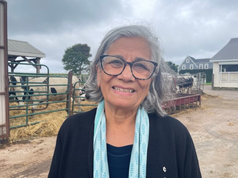 Ontario senator Ratna Omidvar smiles for a photo standing on a farm in front of dairy cows.