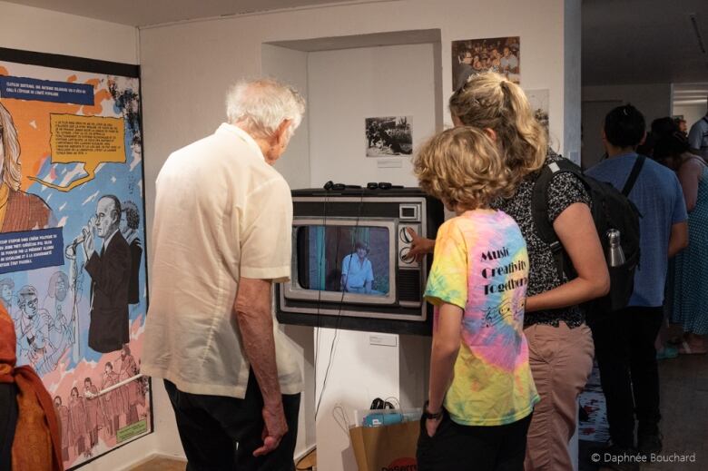 A senior, woman and teen look at an old TV display during an exhibit on the legacy of Salvador Allende's politics in Quebec. 