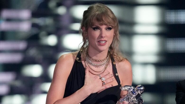 A woman holds a silver trophy and rests her hand on her heart.